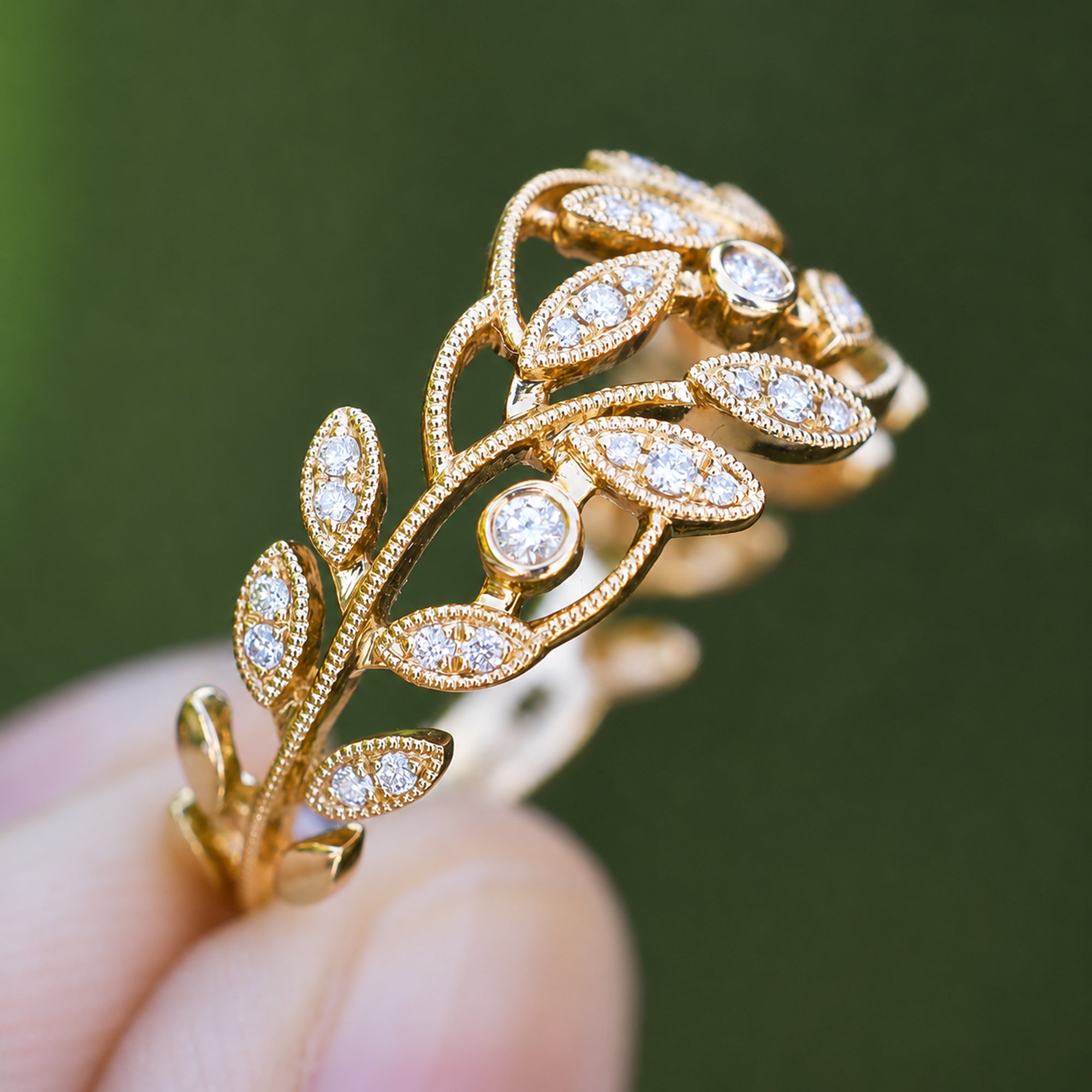 Gold ring with diamond leaves held by a hand against a green background