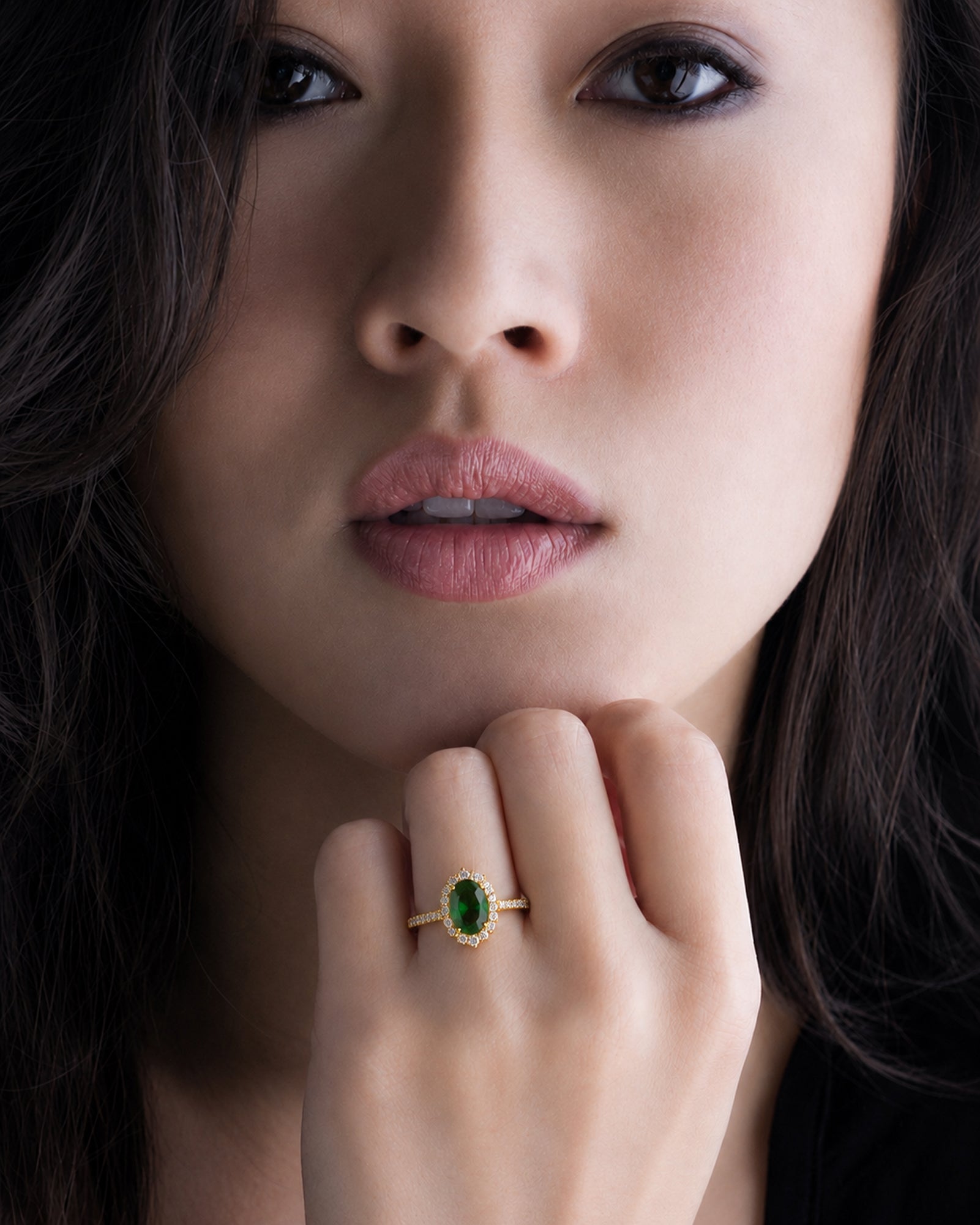 Close-up of a woman's face with a green gemstone ring on her finger.