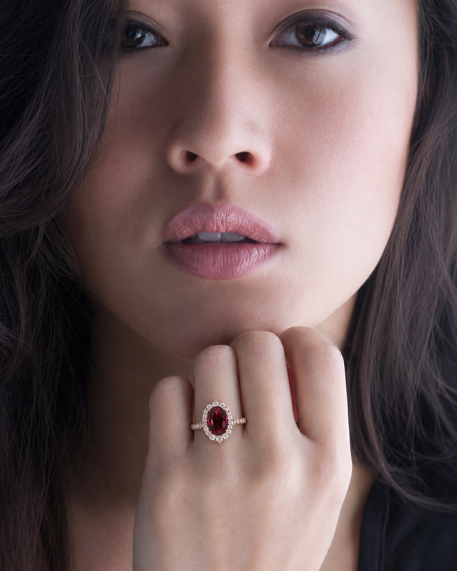 Close-up of a woman's face with a red gemstone ring on her finger.