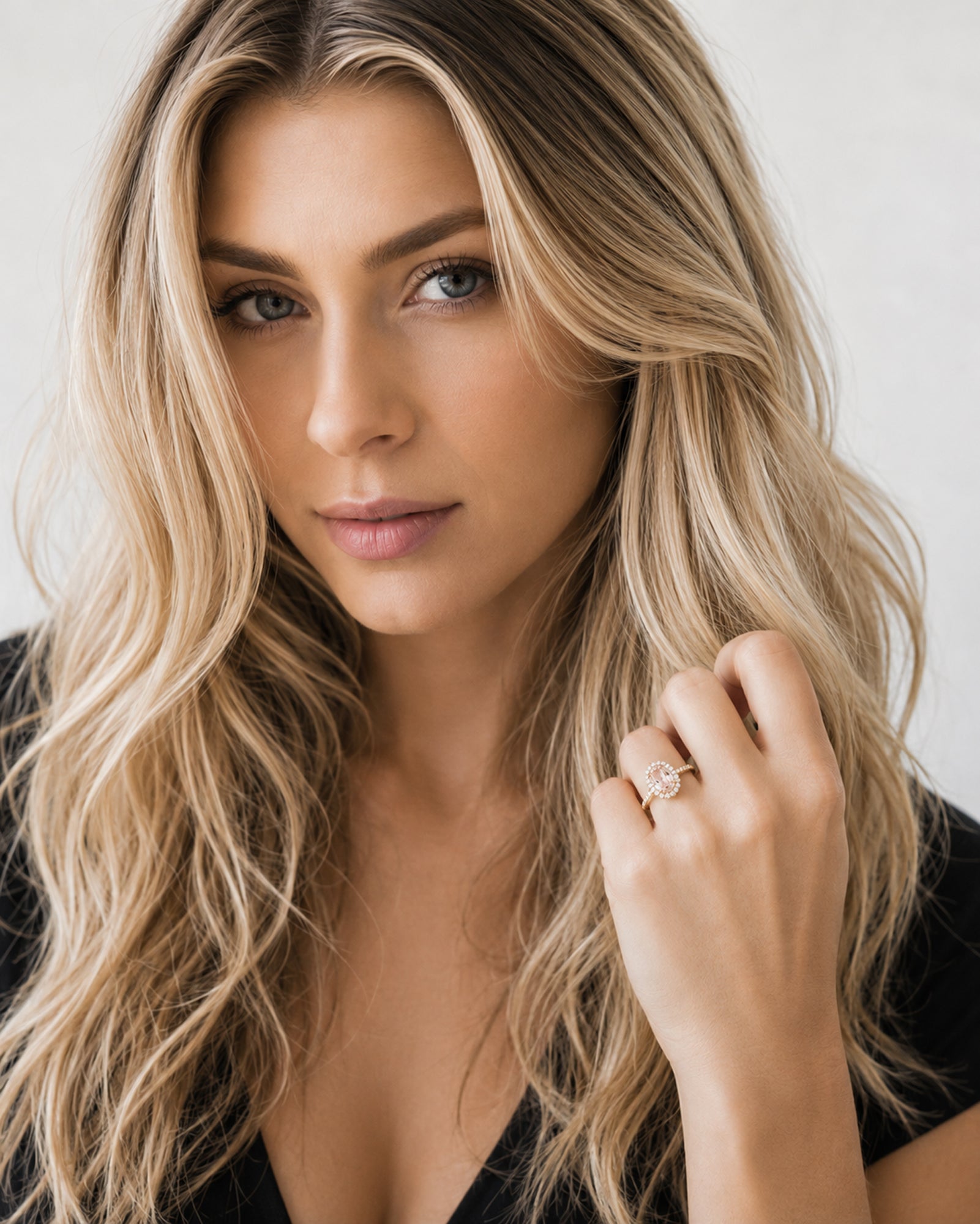 Woman with long blonde hair wearing a ring on her finger against a neutral background