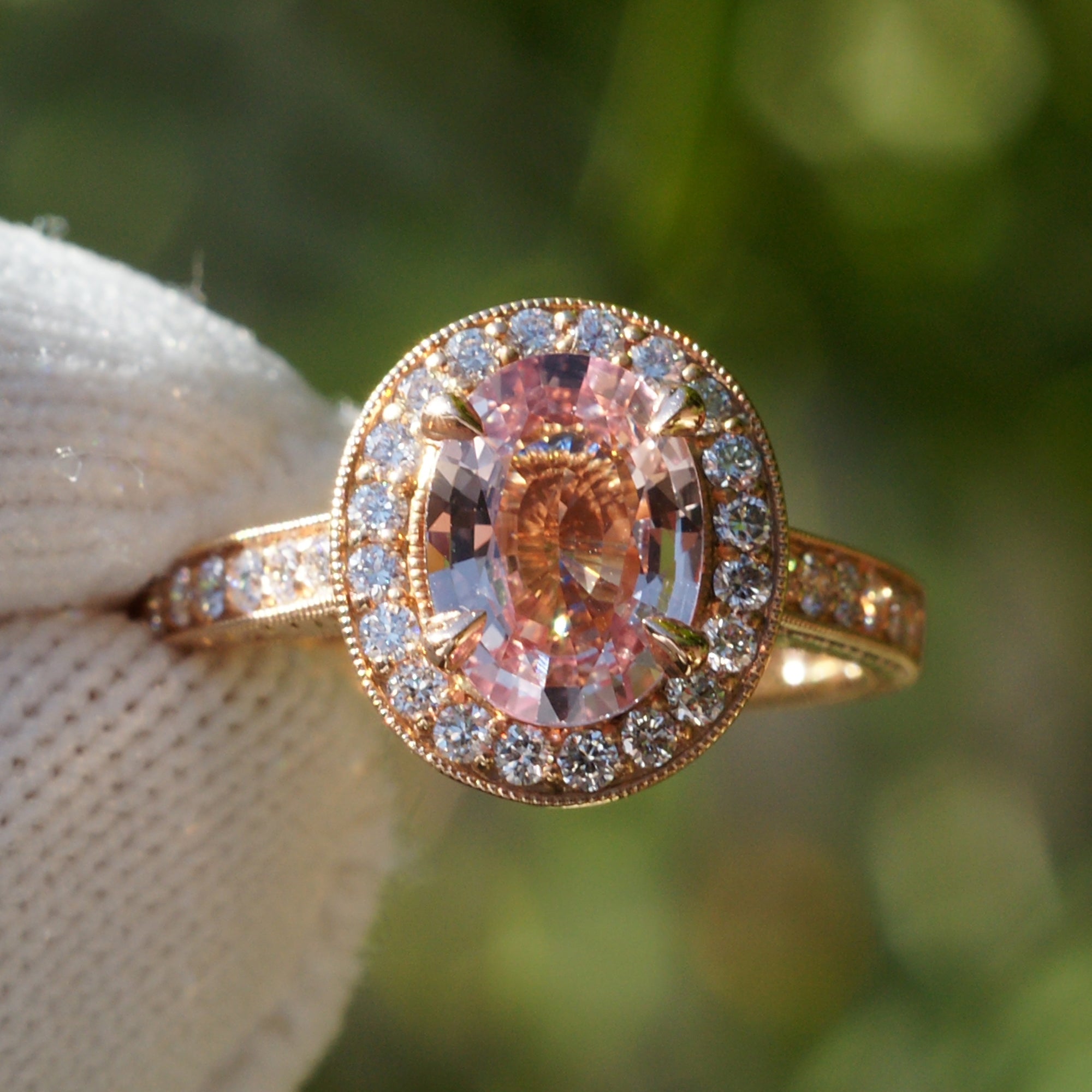 Oval pink sapphire with diamond halo engagement ring on a vintage hand carved rose gold setting