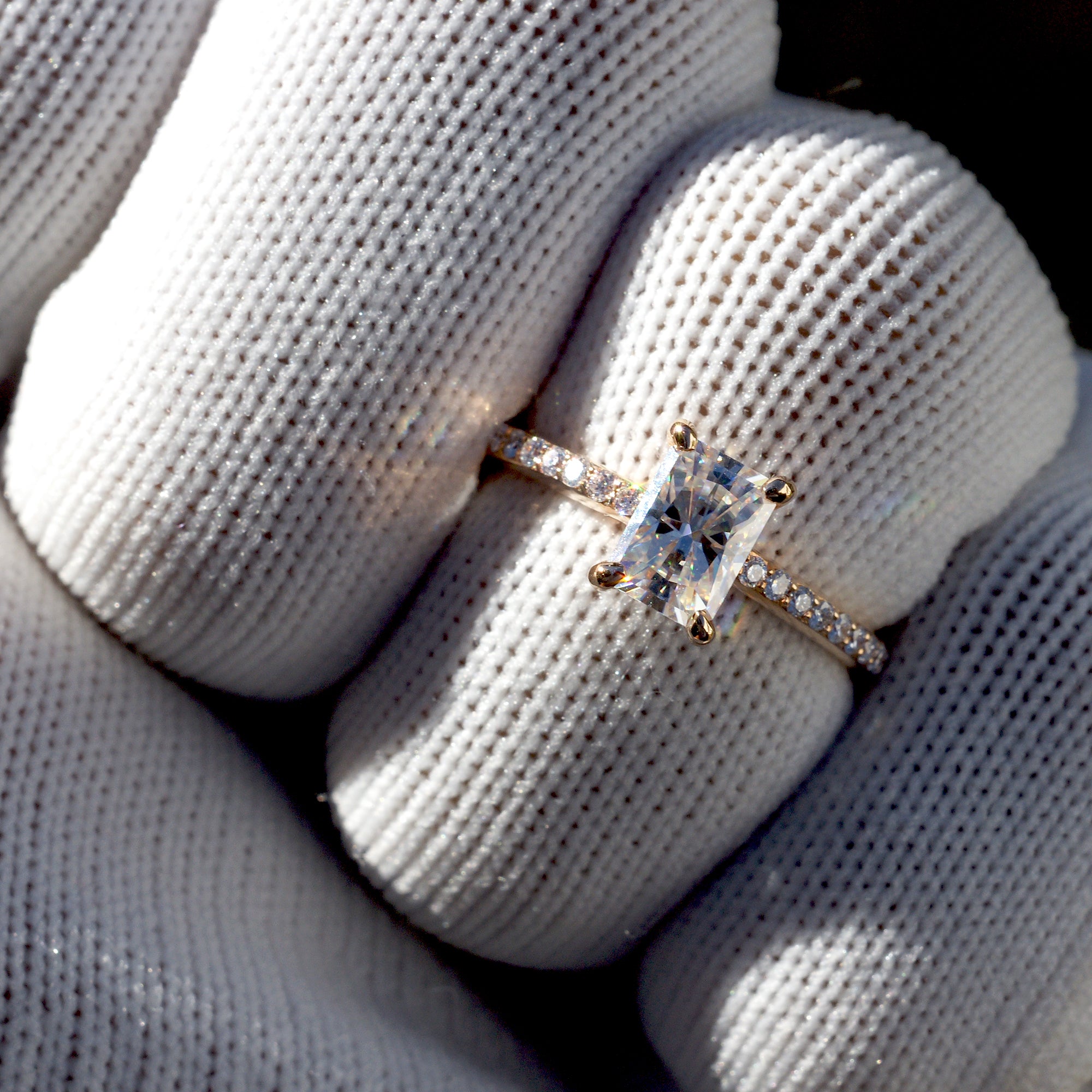 Radiant cut moissanite ring in rose gold with diamond accent on band, on finger