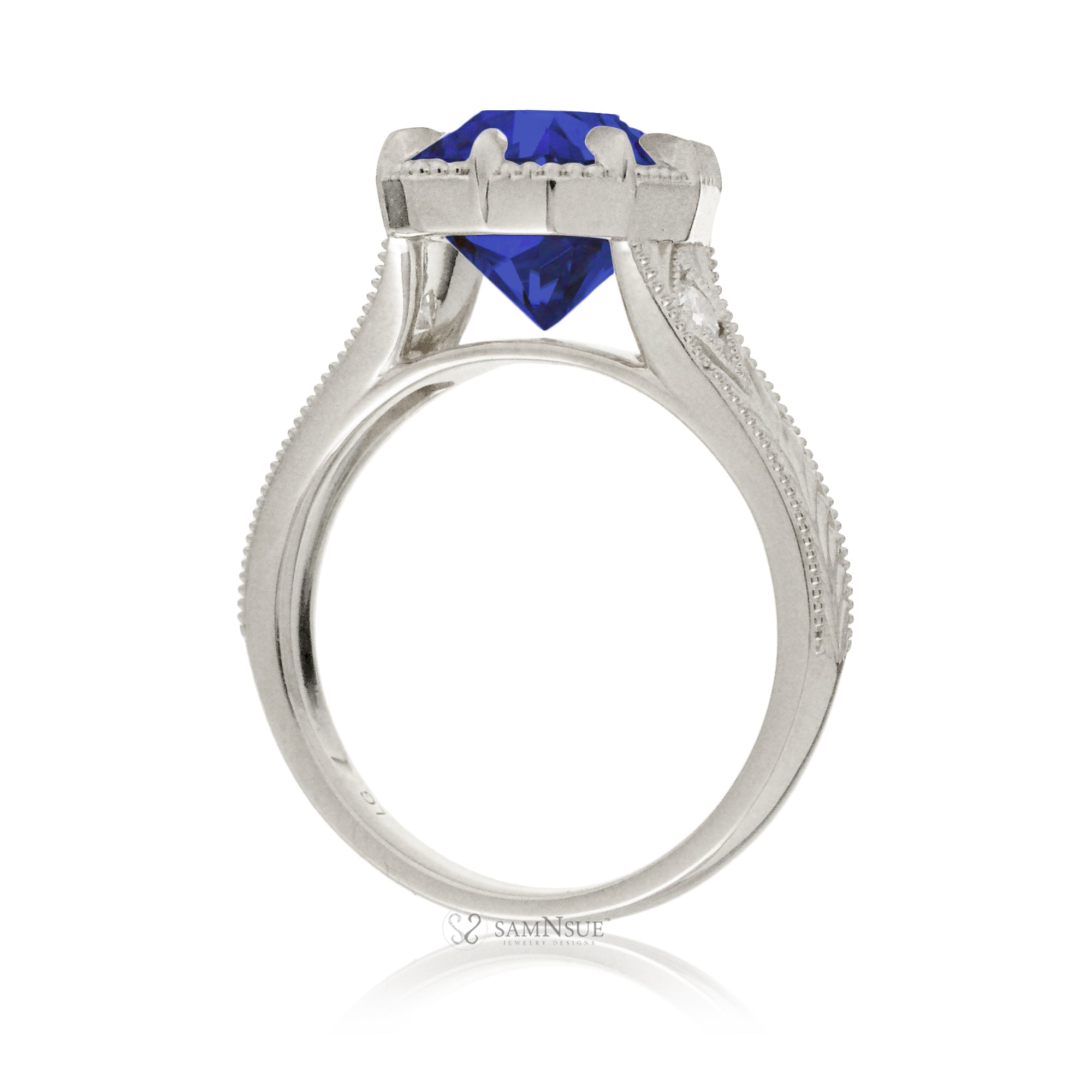 A cushion cut blue sapphire glimmers at the heart of this vintage-inspired engagement ring, set in polished white gold. The detailed band features hand-carved artistry, enhancing the antique character and timeless appeal.