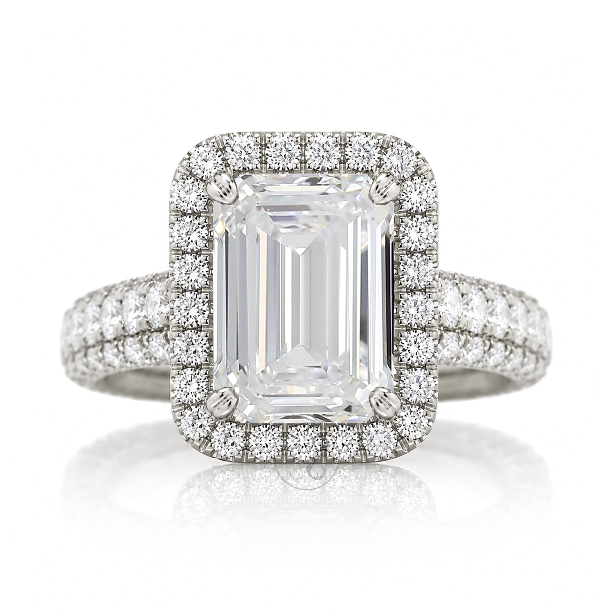 An emerald-cut halo ring featuring a large clear center stone surrounded by a double halo of smaller round stones, with a pavé-set band, shown on a white background with a soft reflection.
