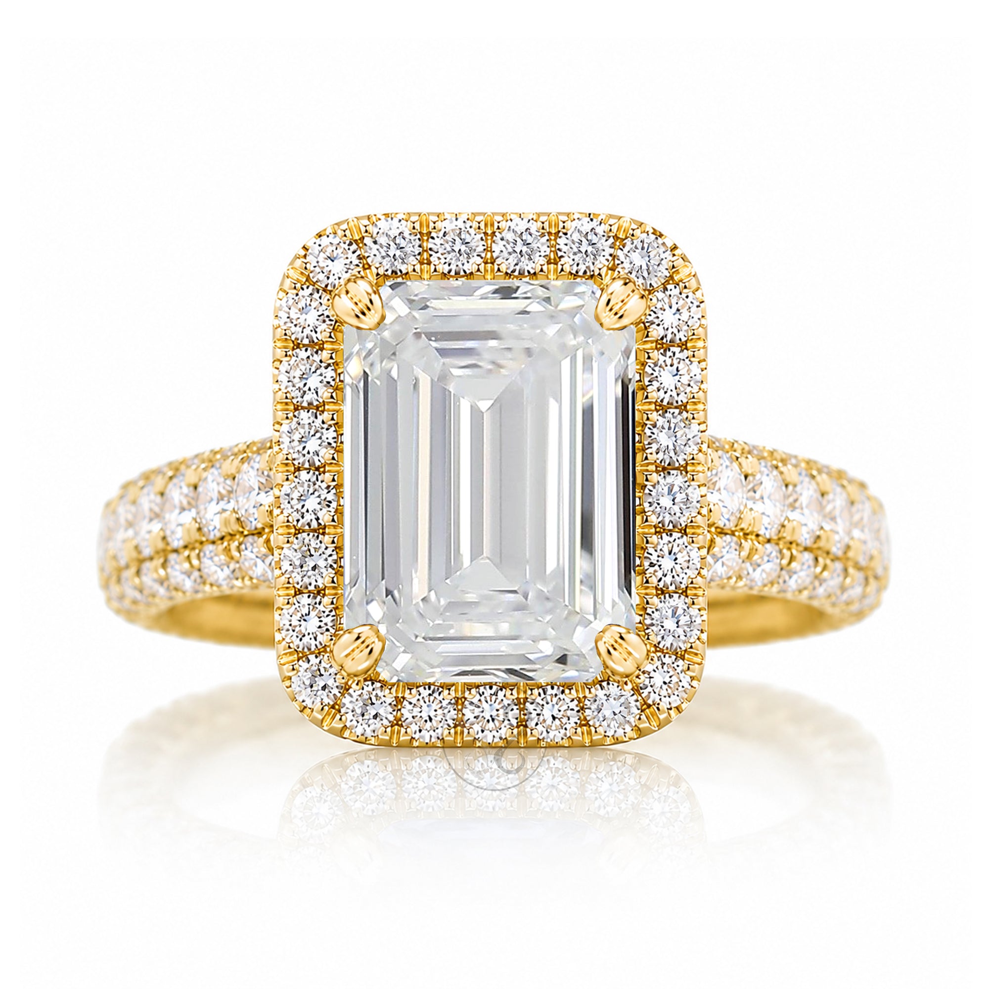 A yellow gold engagement ring featuring a large rectangular emerald-cut center stone surrounded by a double halo of small round diamonds, with additional diamonds set along the band, shown on a white background with a soft reflection.