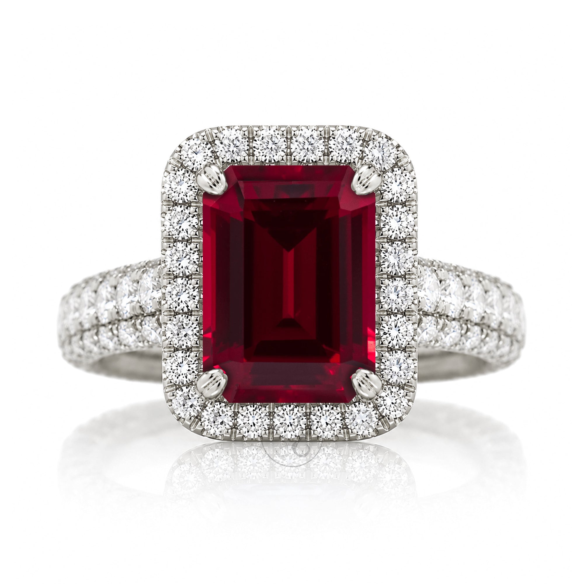A luxury emerald-cut ruby ring with a double halo of small diamonds and a diamond-encrusted band, set in a silver-toned metal on a white background with a soft reflection.