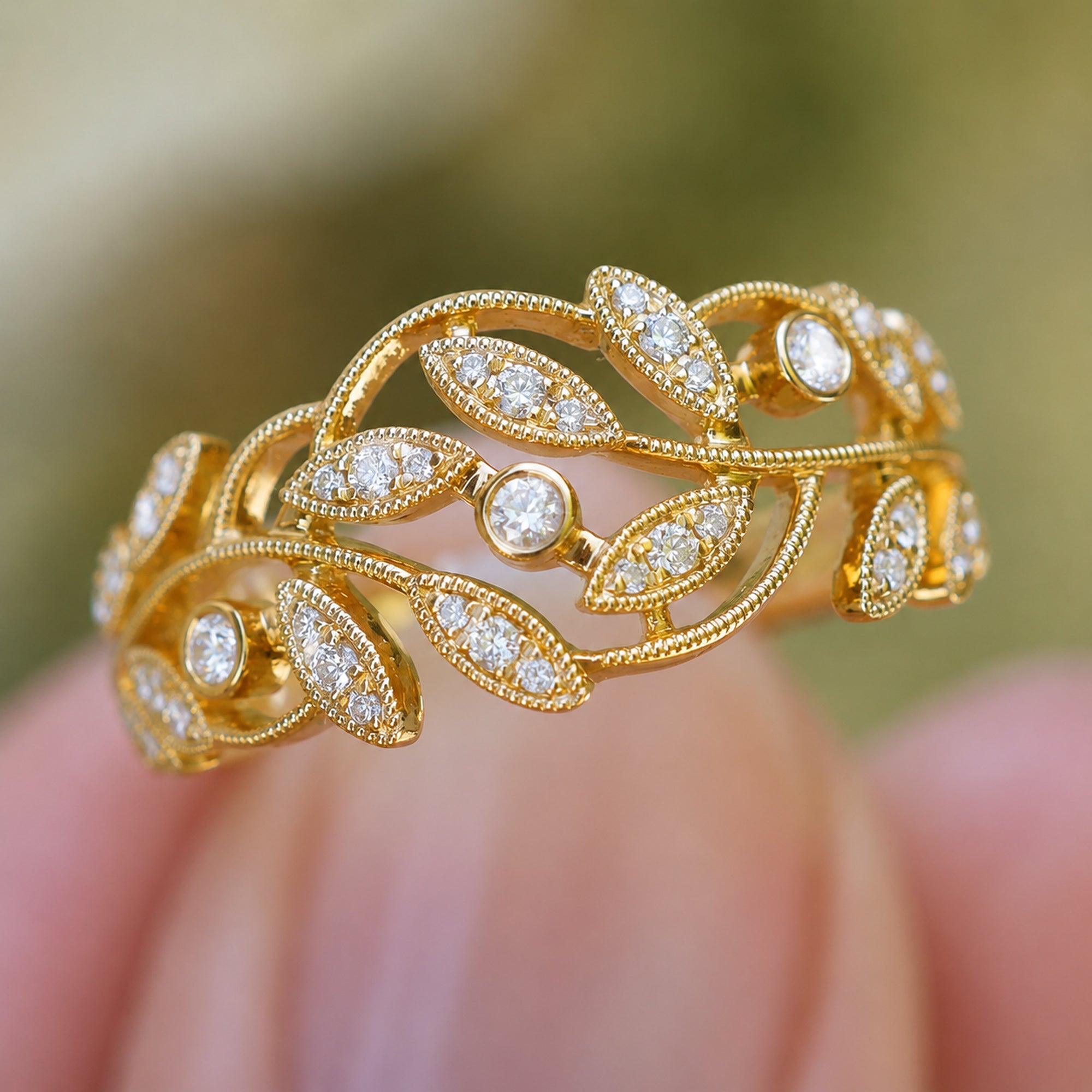 Gold ring with diamond accents held between fingers against a blurred background
