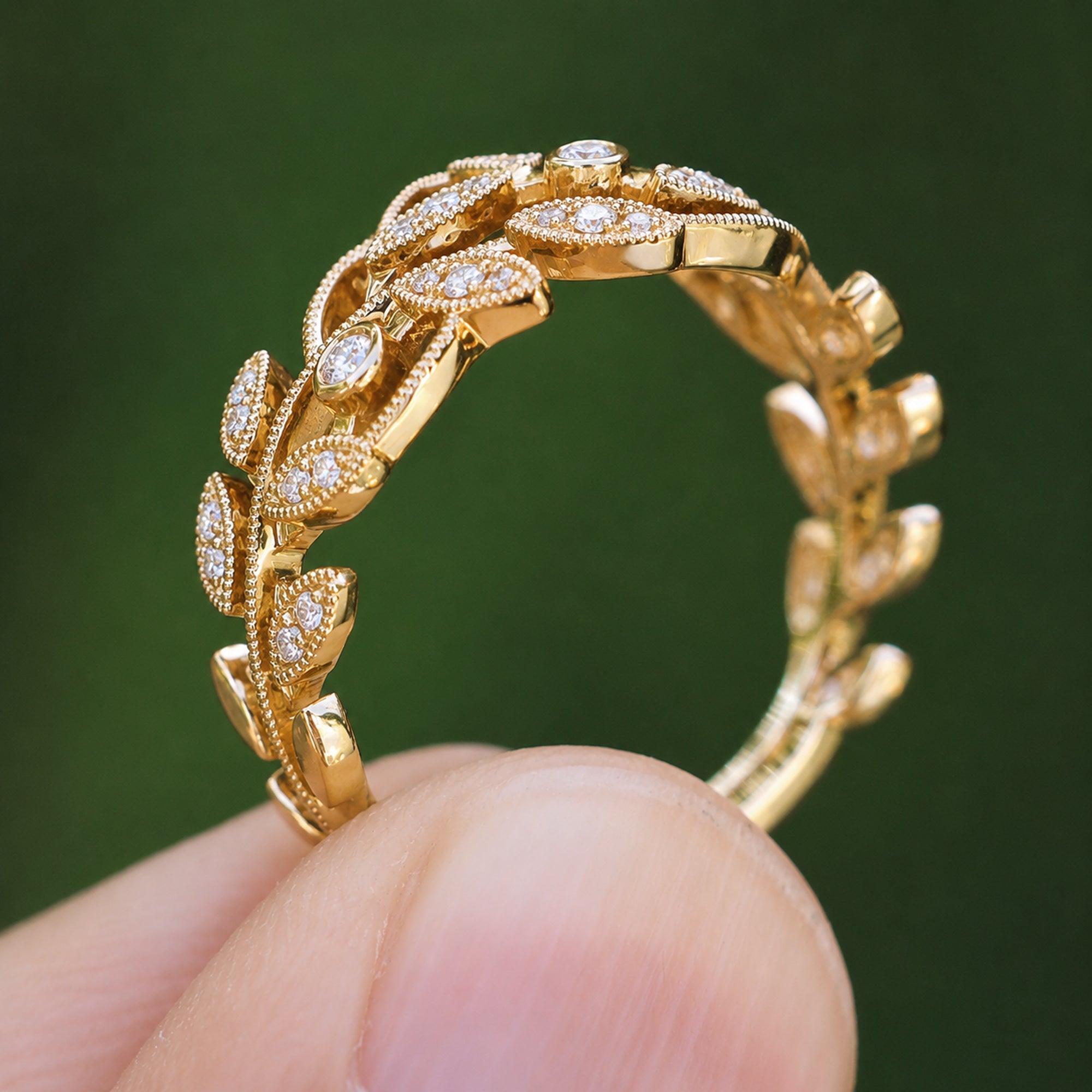 Gold ring with leaf design held by a hand against a green background