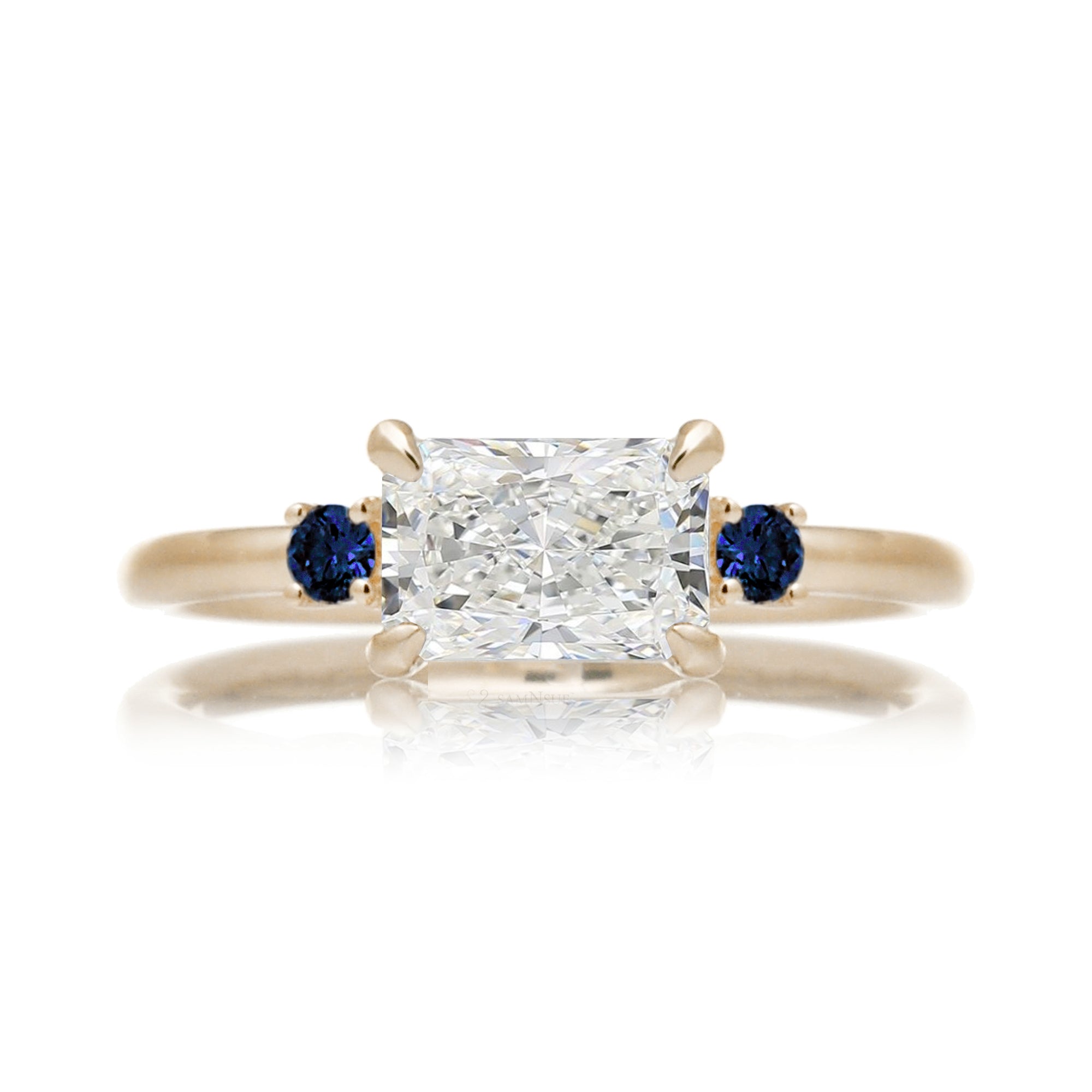 east-west radiant cut lab-grown diamond threestone ring with side blue sapphires yellow gold