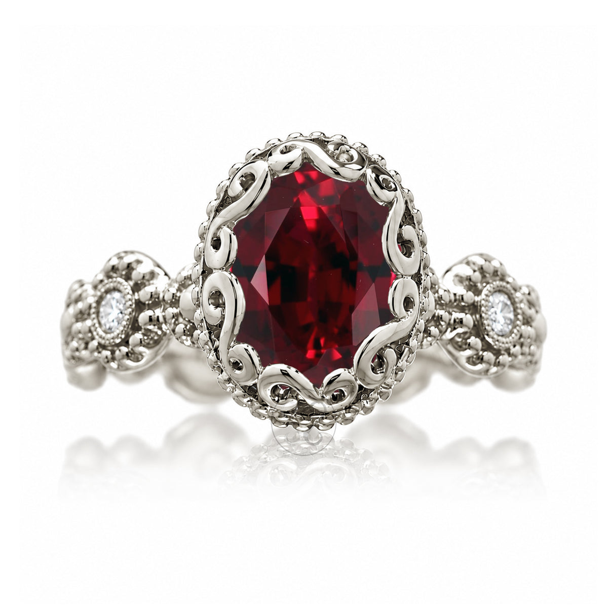 An ornate silver filigree ring featuring a large oval-cut deep red gemstone in the center, with small clear accent stones on the shoulders, set against a clean white background with a soft reflection.