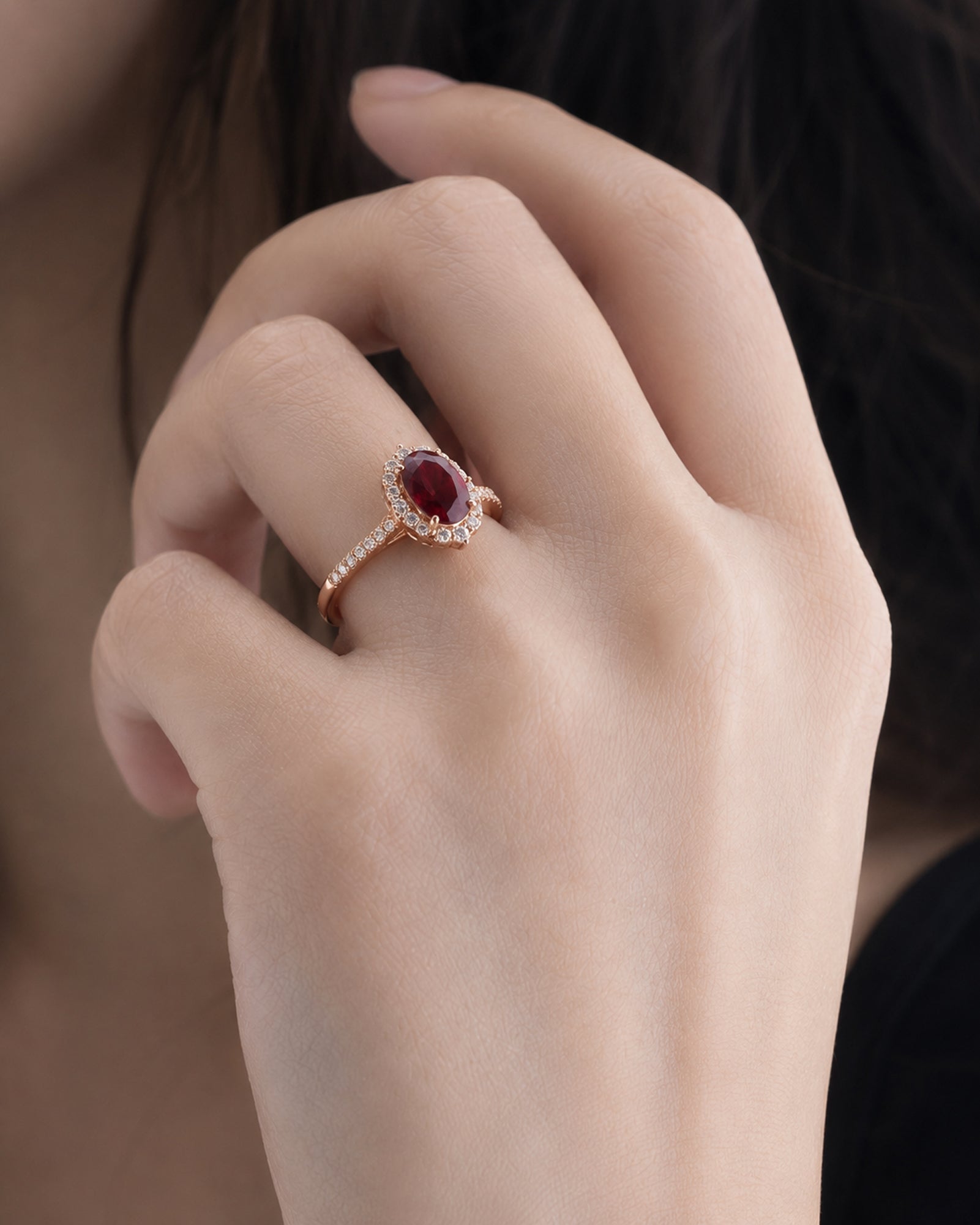 Hand wearing a ring with a red gemstone on a blurred background