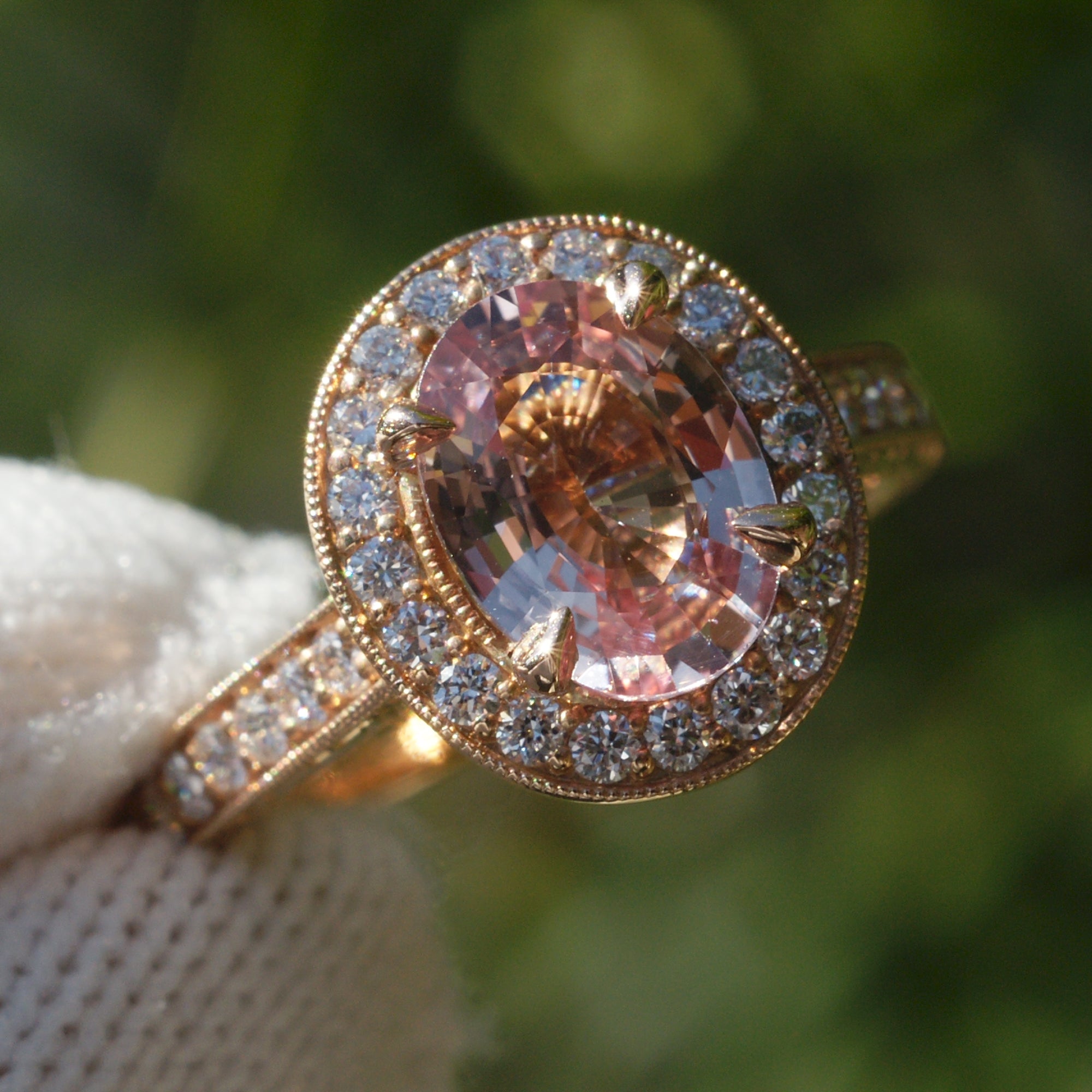 Oval pink sapphire with diamond halo engagement ring on a vintage hand carved rose gold setting