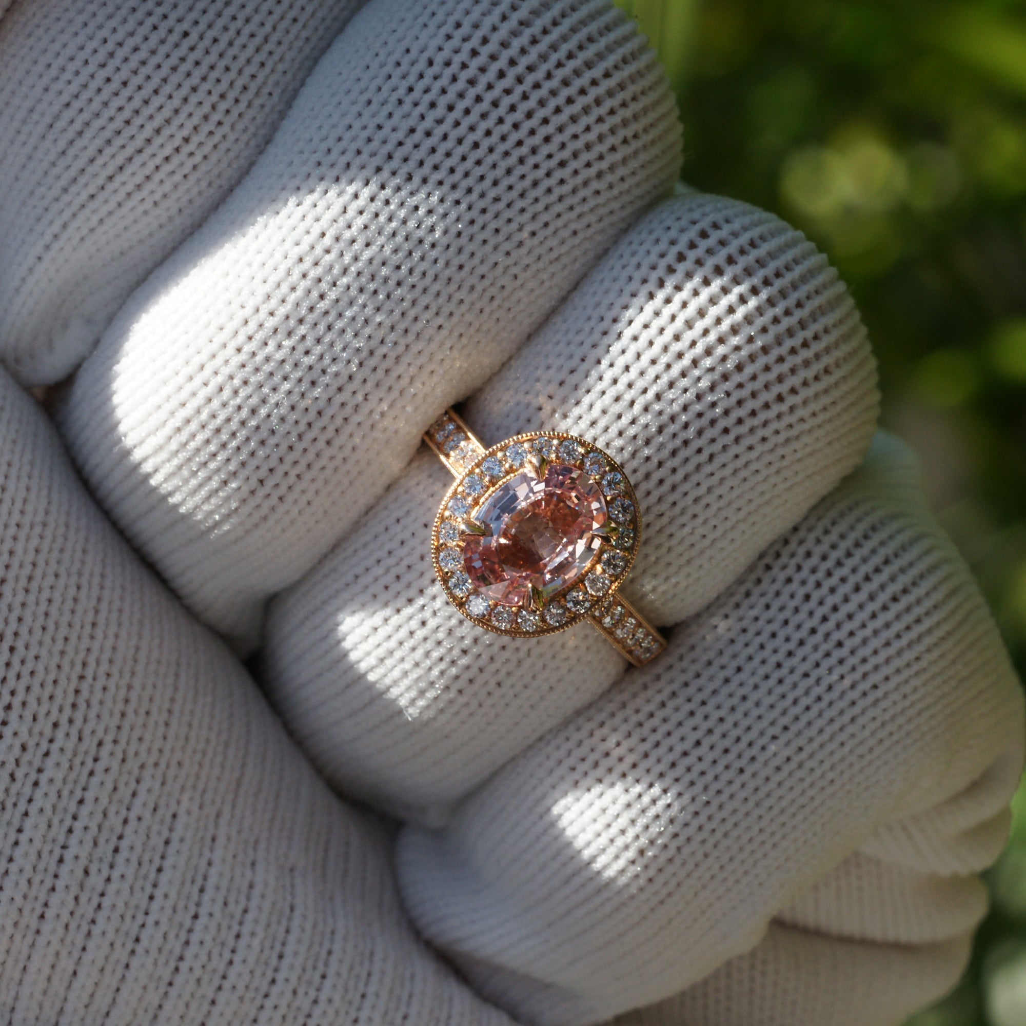 Oval pink sapphire with diamond halo engagement ring on a vintage hand carved rose gold setting