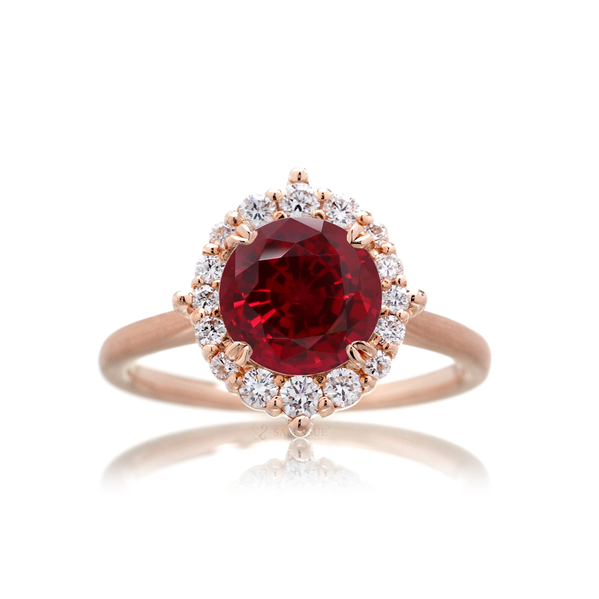 Rose gold ring with a red gemstone and diamond accents on a white background