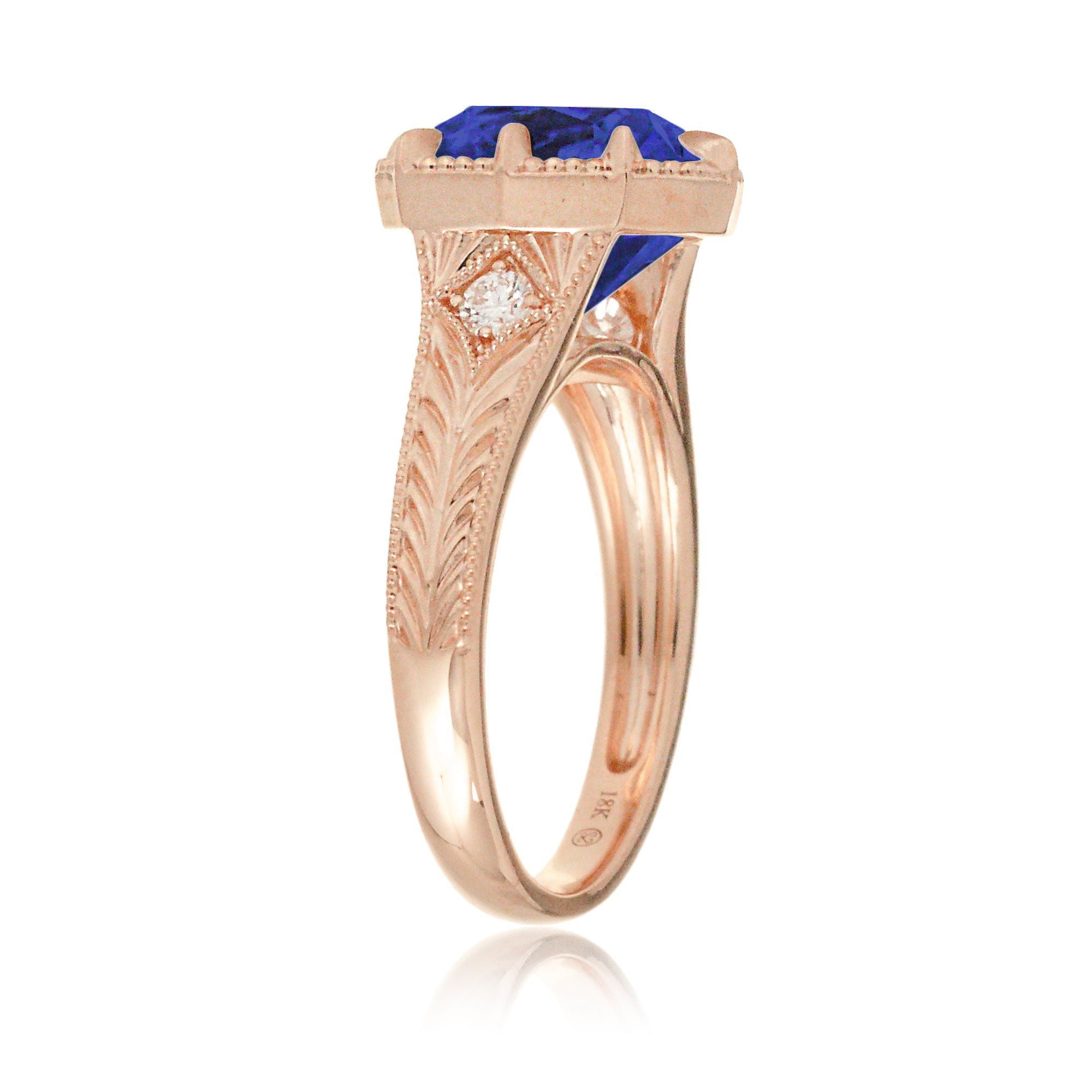 A cushion cut blue sapphire glimmers at the heart of this vintage-inspired engagement ring, set in polished rose gold. The detailed band features hand-carved artistry, enhancing the antique character and timeless appeal.