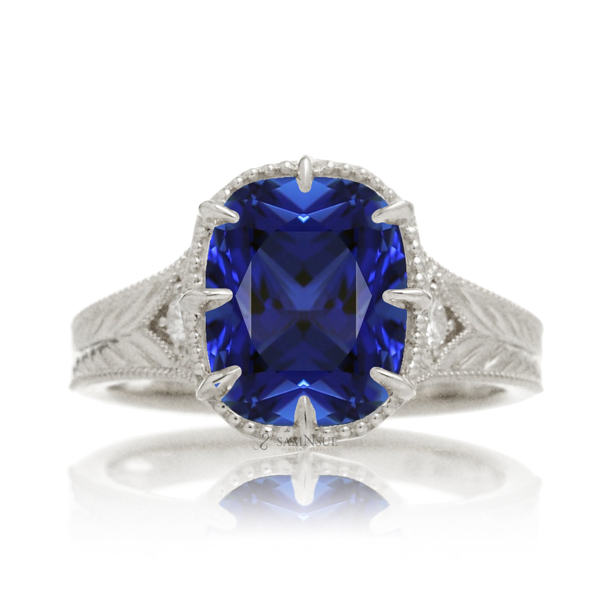 A cushion cut blue sapphire glimmers at the heart of this vintage-inspired engagement ring, set in polished white gold. The detailed band features hand-carved artistry, enhancing the antique character and timeless appeal.
