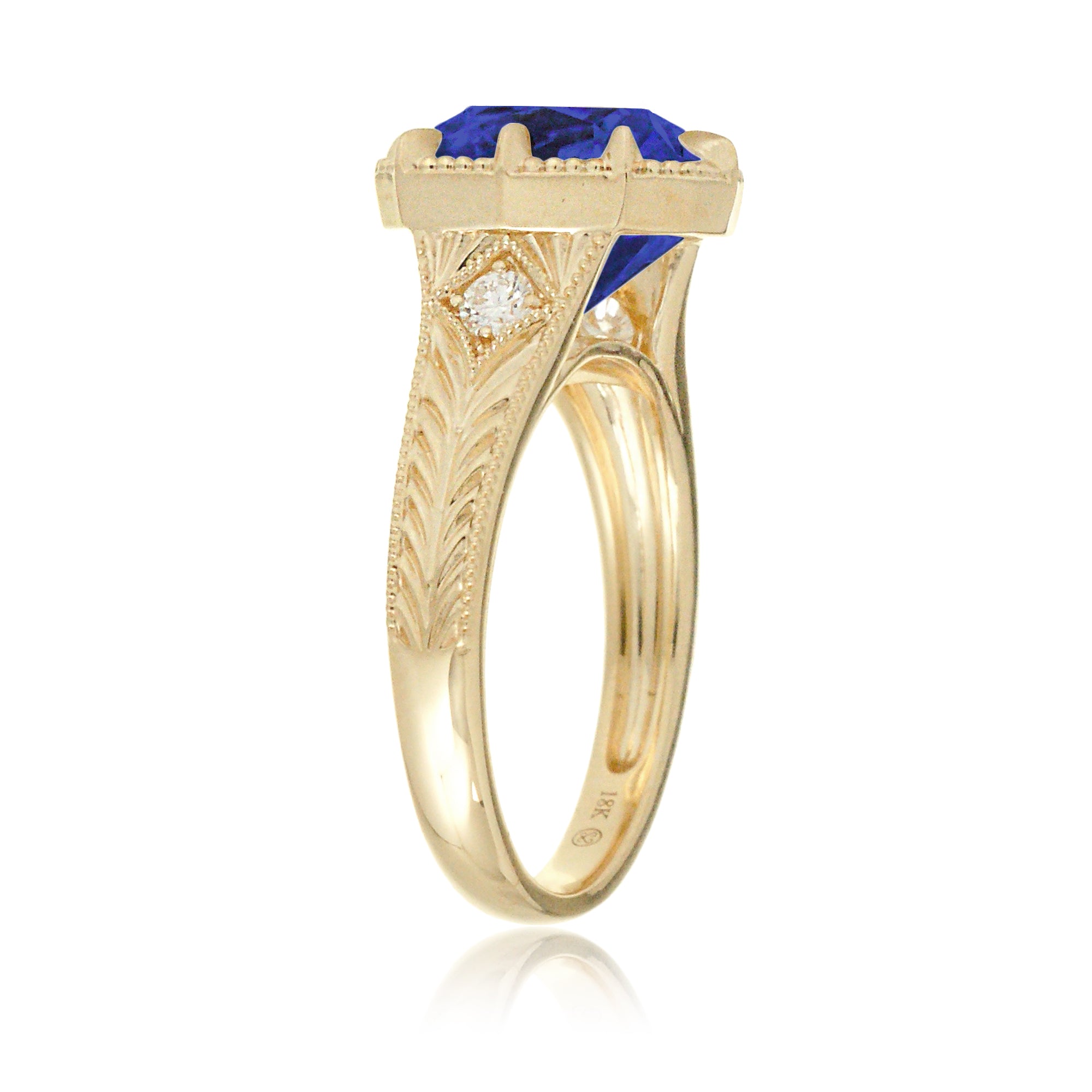 A cushion cut blue sapphire glimmers at the heart of this vintage-inspired engagement ring, set in polished yellow gold. The detailed band features hand-carved artistry, enhancing the antique character and timeless appeal.