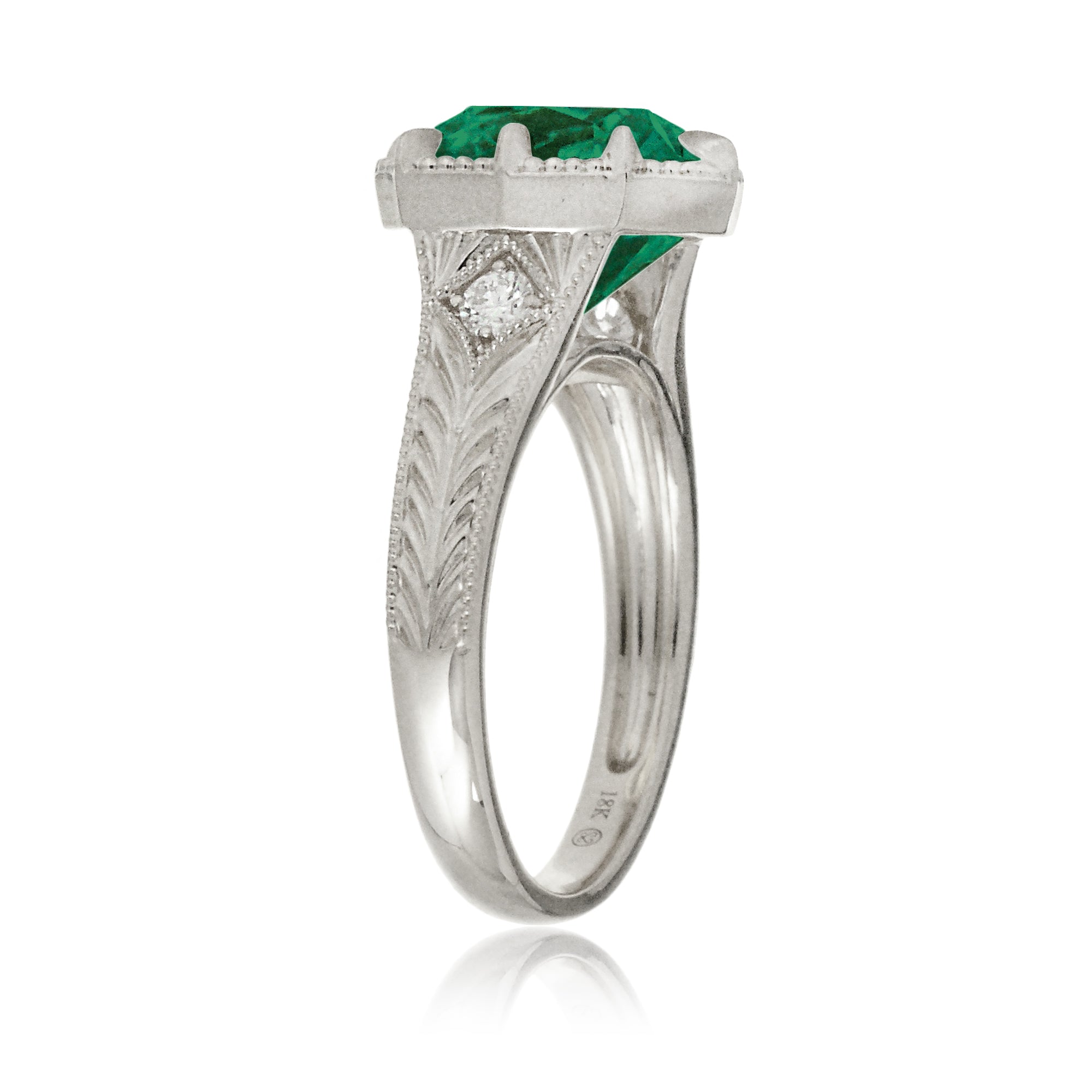This heirloom-style ring showcases a cushion-shaped emerald. The white gold setting, paired with intricate engraving, creates a romantic design reminiscent of old-world glamour.