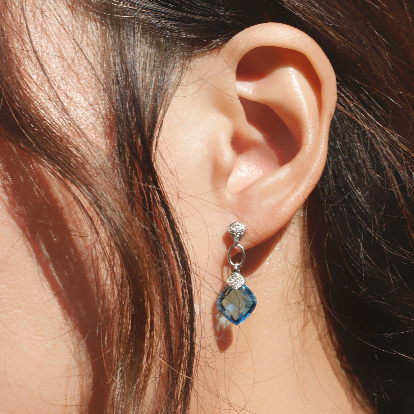 Close-up of an ear wearing a blue gemstone earring with a blurred background