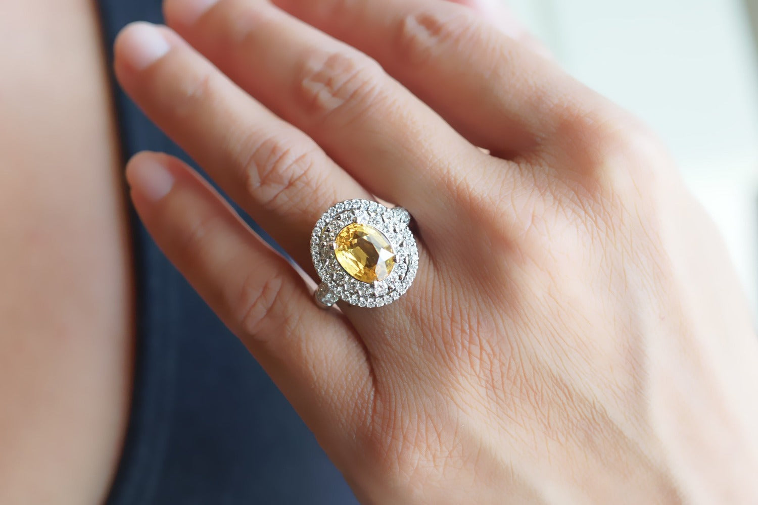 Oval yellow sapphire ring with a double diamond halo on a hand